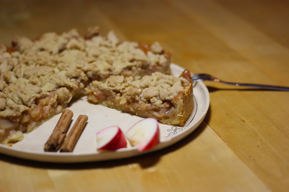 Ein Apfelkuchen mit Zimtstangen und Apfelstücken garniert.
